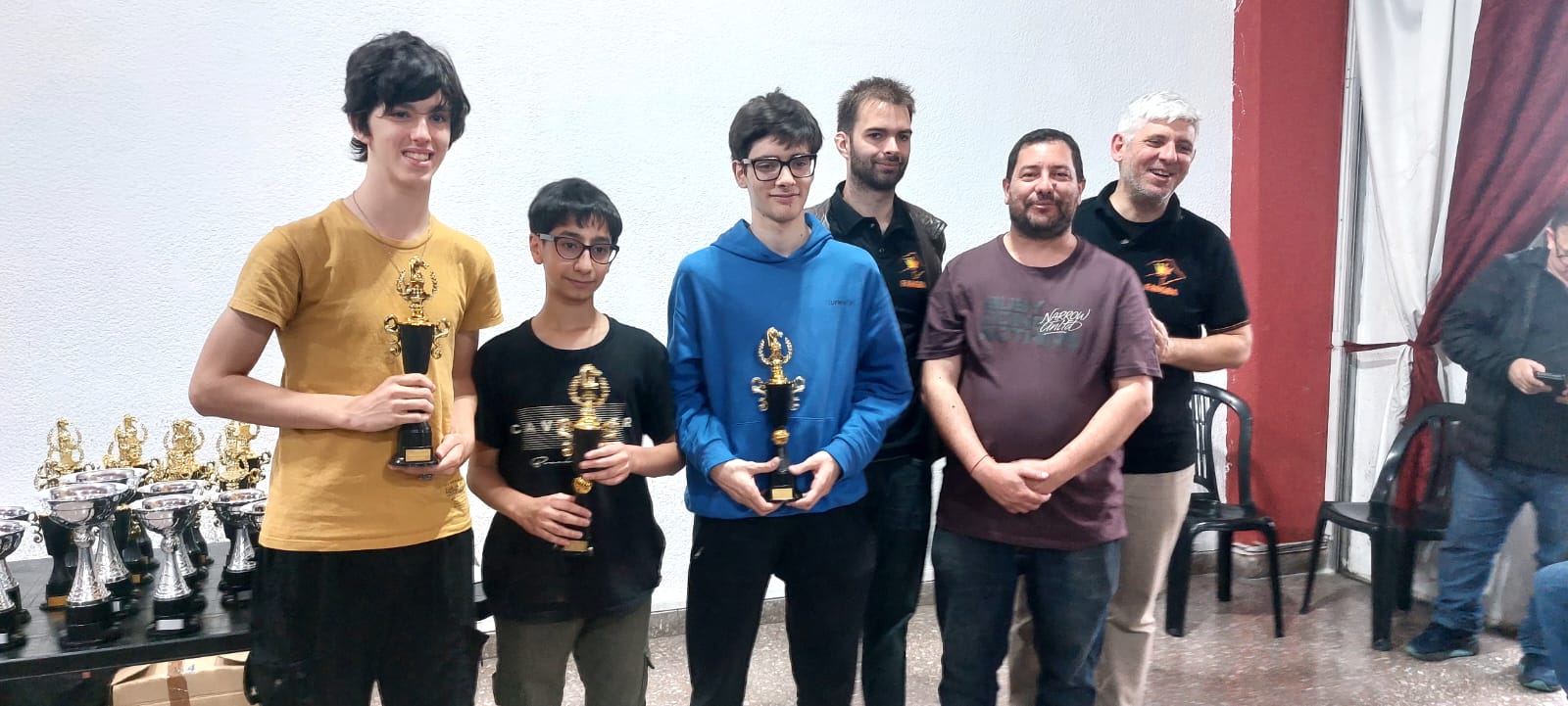 Trofeos para los campeones Miguel Fernández, Facundo Saglietti e Iván Scheinson, junto al profe Juan Pablo Nesich de JuegoCiencia y autoridades de la Federación